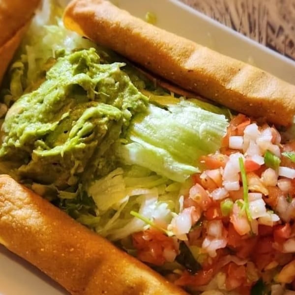 Crispy taquitos with guacamole, shredded lettuce, and pico de gallo on a white plate.