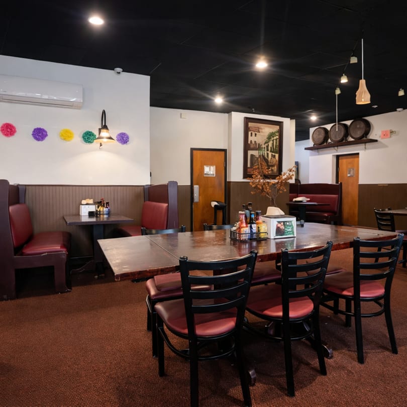 Restaurant interior with red booths, dark tables, black chairs, and colorful wall decorations.