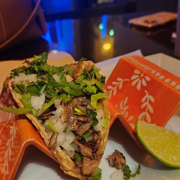 A delicious taco with meat, onions, and cilantro, served in an orange holder with a lime wedge.