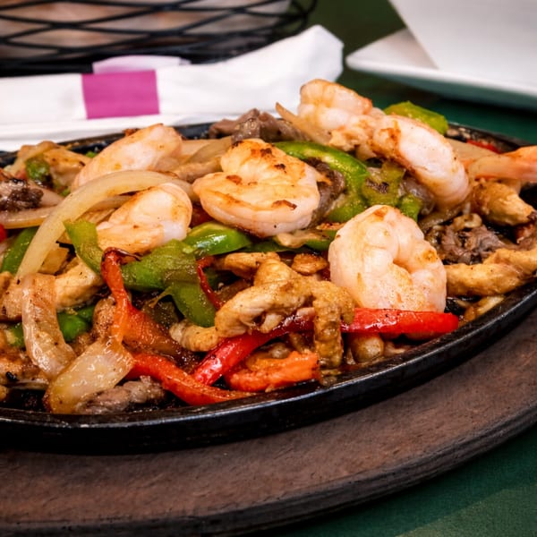 Sizzling fajitas with shrimp, chicken, onions, and bell peppers on a cast iron platter.