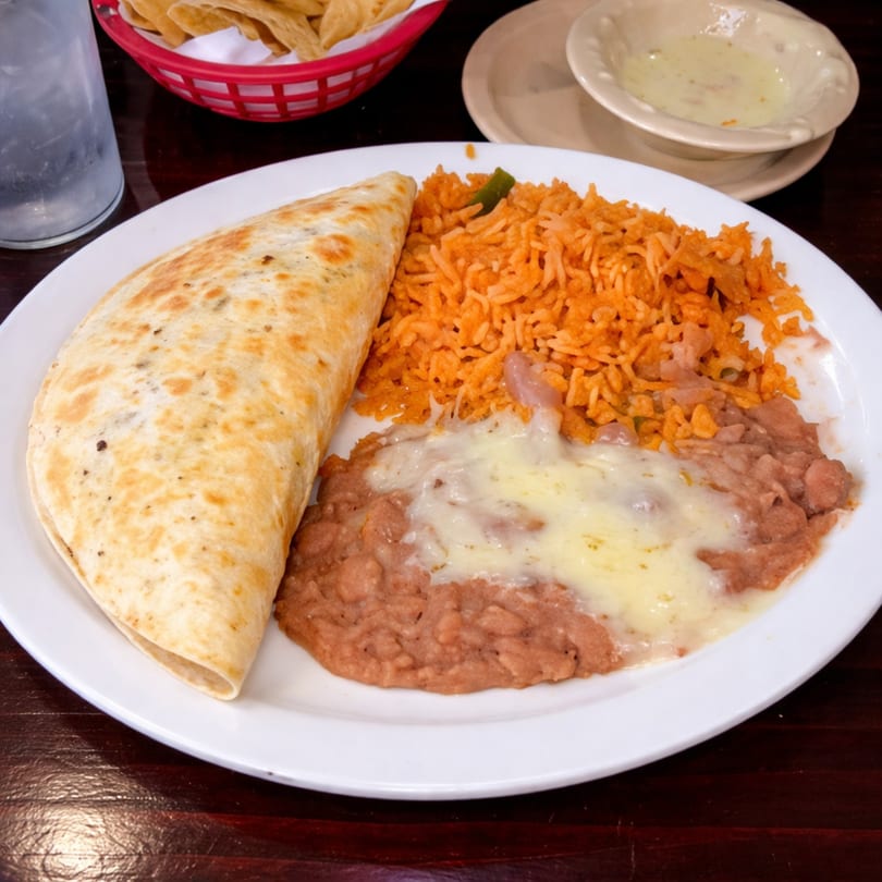 A quesadilla, red rice, and refried beans with melted cheese on a white plate.